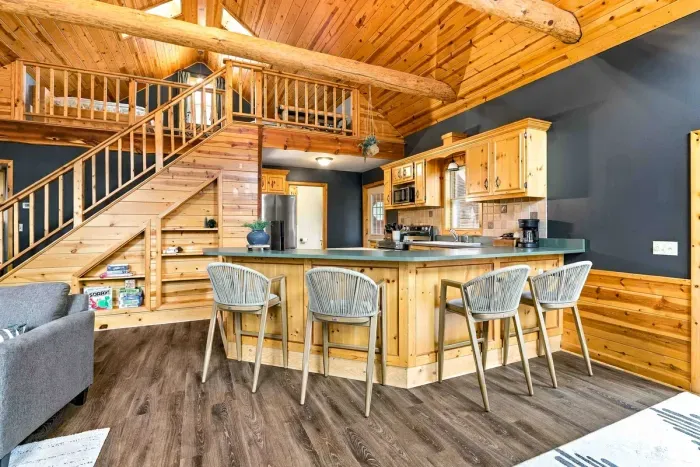 Gather around the expansive breakfast bar with seating for four in this open-concept kitchen, featuring modern appliances and custom wood cabinetry beneath soaring vaulted ceilings.