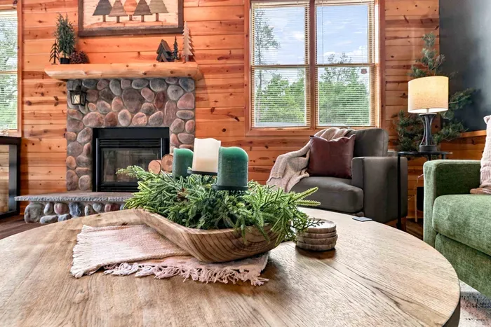 Gather around the focal stone fireplace in this inviting great room, framed by rustic log beams, a flat-screen TV, and plush lounge seating.