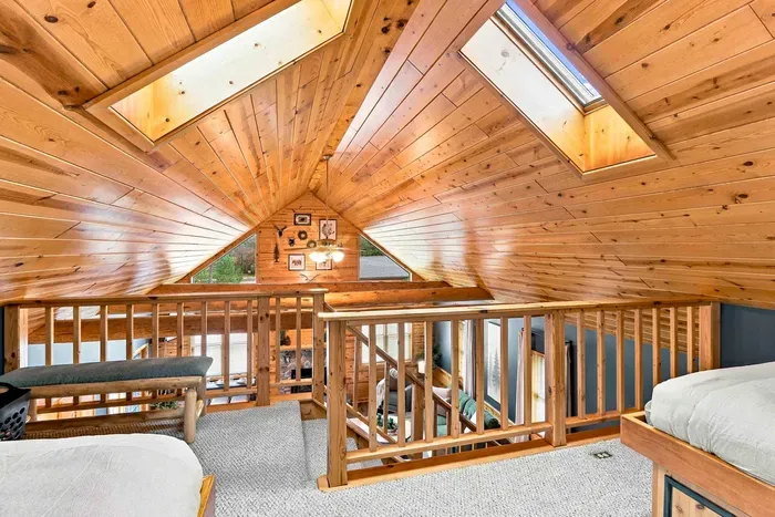 Cozy up in this charming loft bedroom featuring twin beds with built-in storage drawers and a stylish wooden dresser beneath warmth-filled wood ceilings.