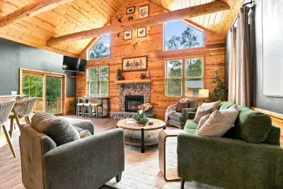 Unwind in this warm, open living area featuring vaulted log-beam ceilings, a cozy stone fireplace, comfortable sofa seating, and a mounted TV.