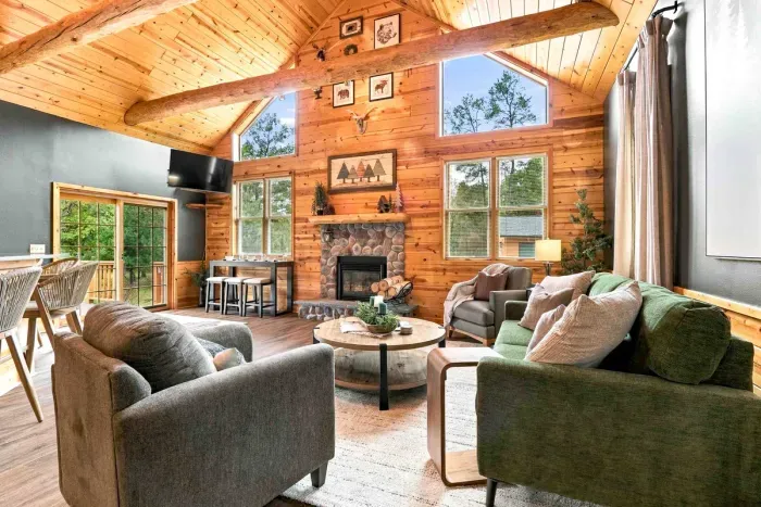 Unwind in this warm, open living area featuring vaulted log-beam ceilings, a cozy stone fireplace, comfortable sofa seating, and a mounted TV.