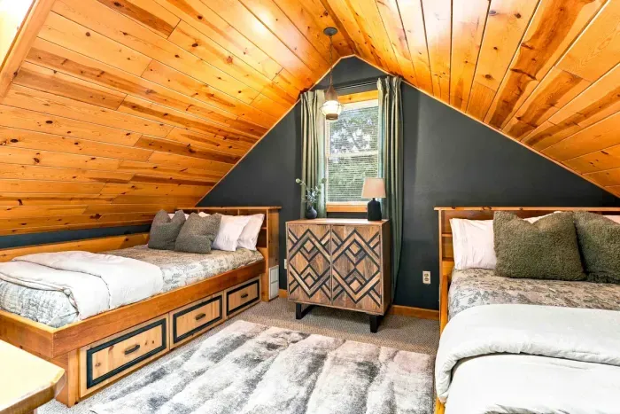Sleep comfortably under angled pine ceilings in a cozy loft equipped with twin beds, under-bed storage drawers, and a patterned accent dresser.