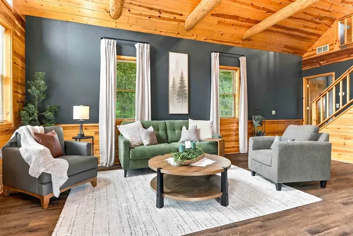 Gather around the focal stone fireplace under rustic log beams, featuring comfortable sofa seating and a stylish coffee table.
