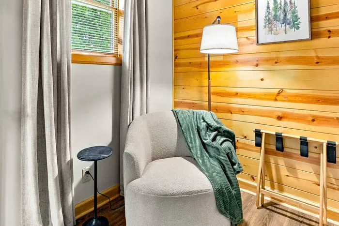 Settle into this peaceful bedroom nook with comfortable accent seating and a folding luggage rack set against warm wood paneling.