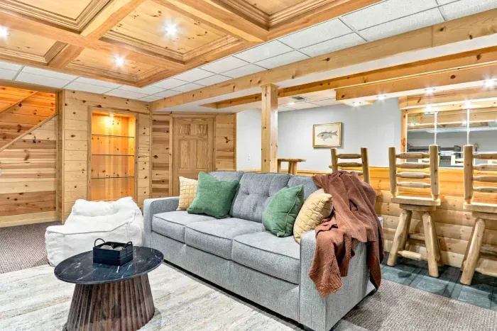 Kick back in the cozy lower-level lounge equipped with a large smart TV, comfortable sofa seating, a plush beanbag chair, and a rustic high-top bar table.