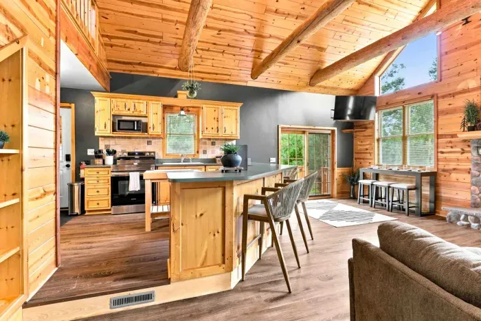 Experience effortless entertaining in this open-concept layout, featuring a fully equipped kitchen, large breakfast bar with seating, and a secondary dining counter beneath soaring log-beam ceilings.