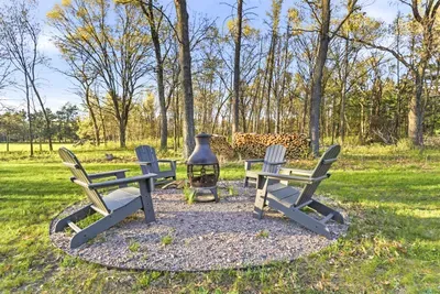 Outdoor firepit area with Adirondack seating, stacked firewood, and a peaceful wooded backdrop for relaxing evenings.