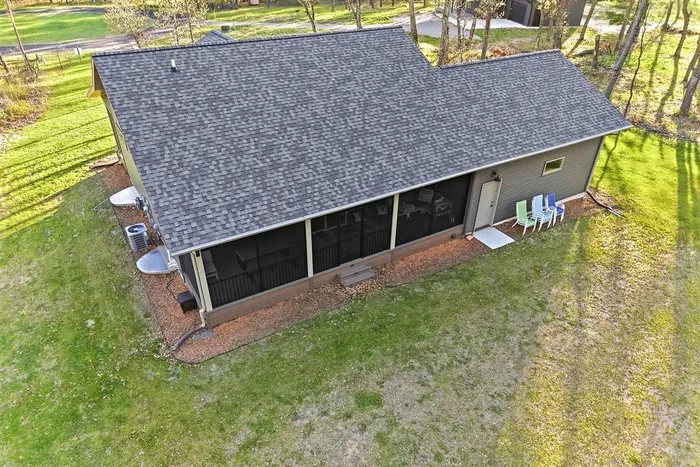 Aerial exterior view highlighting the spacious yard, screened porch, and peaceful wooded setting surrounding the home.