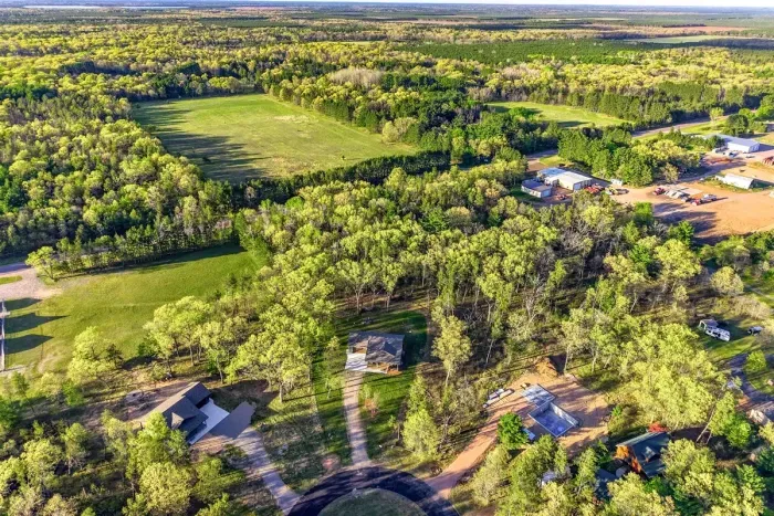 Expansive aerial view showcasing the home’s wooded surroundings, open green space, and peaceful countryside setting.