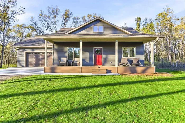 Modern home exterior with a welcoming covered front porch, attached garage, spacious lawn, and peaceful wooded surroundings.