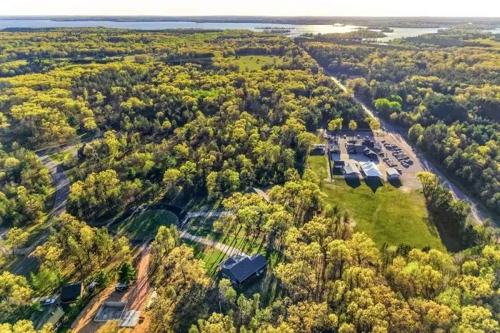 Wide aerial landscape view featuring tree-lined surroundings, open land, and a serene country-style atmosphere.