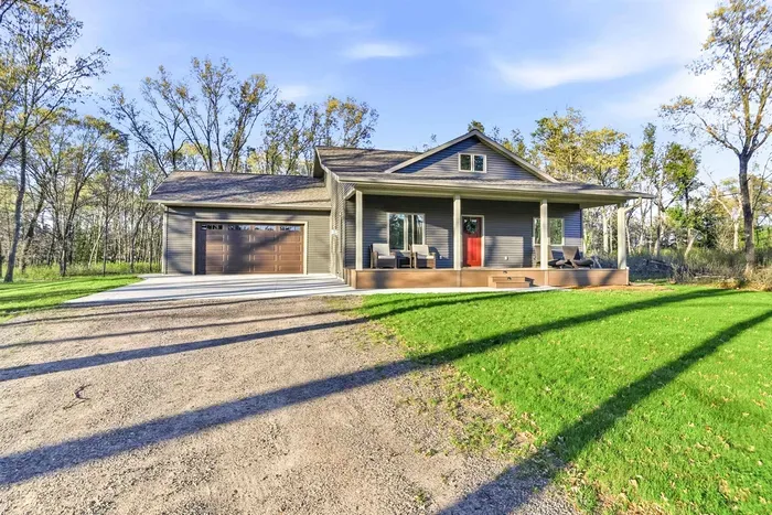 Charming private getaway featuring a covered front porch, attached garage, and open green space surrounded by trees.