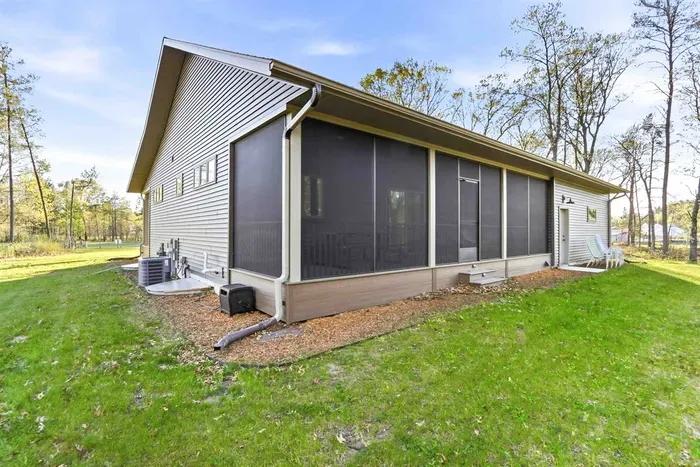 Exterior view featuring a screened porch, open lawn space, and peaceful wooded surroundings for added outdoor enjoyment.