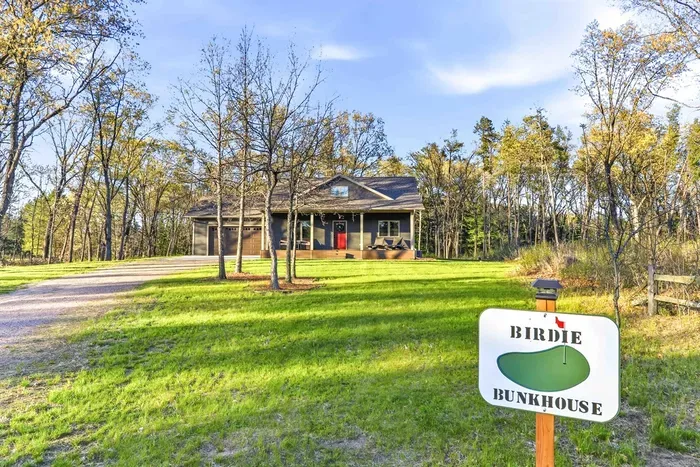Welcoming “Birdie Bunkhouse” exterior with a spacious lawn, wooded surroundings, and a peaceful retreat-style setting.