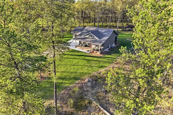 Scenic aerial exterior view showcasing the home tucked among mature trees with open yard space and a quiet, secluded feel.