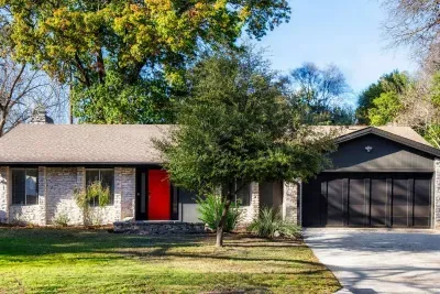 Charming Mid-Mod Exterior: Enjoy a vibrant exterior with lush greenery and a striking deep orange front door!