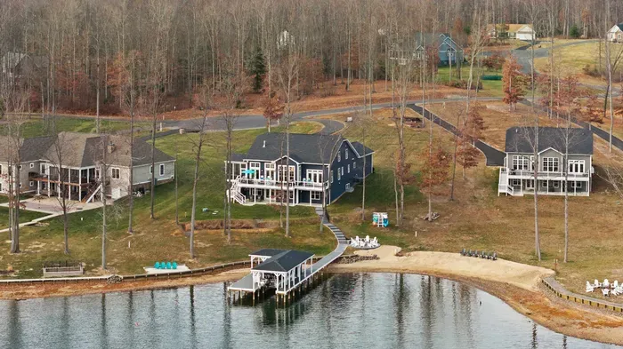 Exterior - Aerial from the lake side shows the blue house, fire pit area, dock, and boathouse together.