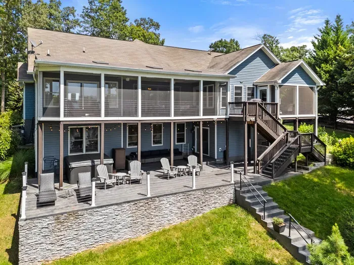 A stunning lakefront home with a spacious screened porch, surrounded by a lush green lawn and a charming stone pathway leading down to the water.