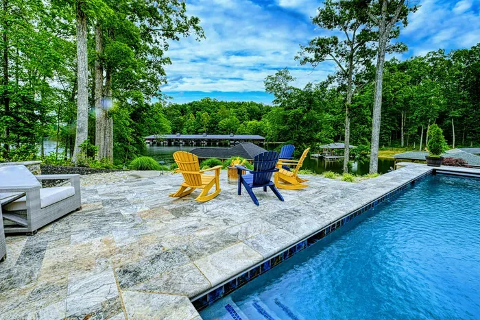 Poolside - Adirondack chairs and poolside lounging on the stone deck, with views of the fire pit area and lake in the background.