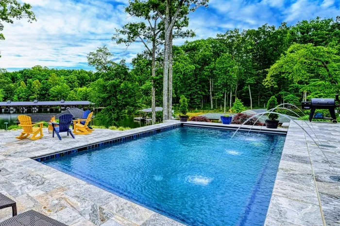 Pool - A resort-style pool with fountain jets, stone surround, and Adirondack chairs sits on the hilltop with lake views through the trees.
