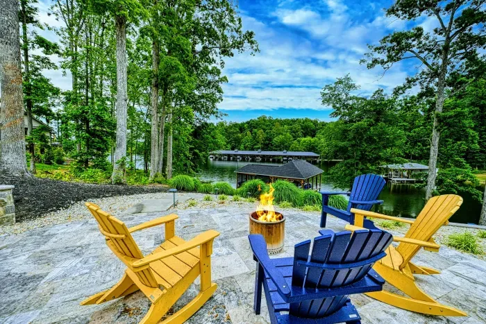Fire Pit - Colorful Adirondack chairs surround a gas fire pit on the stone patio, overlooking the dock and lake below.