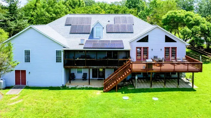 Exterior - Rear of the three-level home with solar panels, wraparound deck, screened porch, and stairs to the yard.
