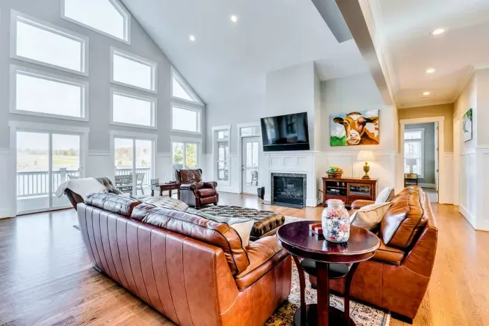 Bright, airy living room with leather seating, a fireplace, and floor-to-ceiling windows showcasing stunning lake views