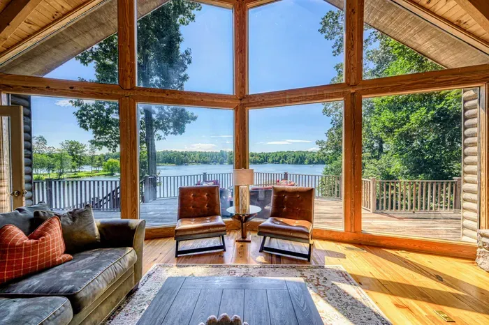 A cozy living room with floor-to-ceiling windows offers breathtaking views of the lake and direct access to a spacious deck.