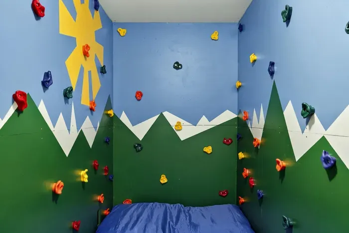 Climbing Wall Detail - Painted mountains and a sunshine mural surround the holds, making this climbing room a highlight for younger guests.