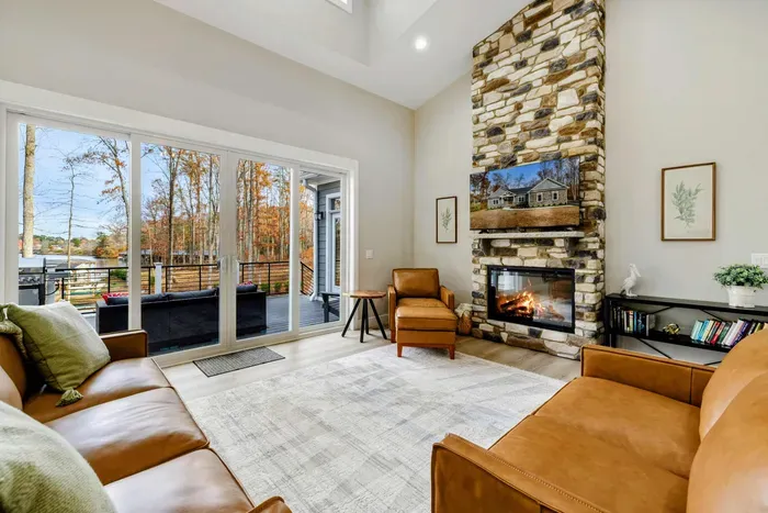 Spacious living room with a stone fireplace, leather seating, and large sliding doors opening to a scenic outdoor deck.
