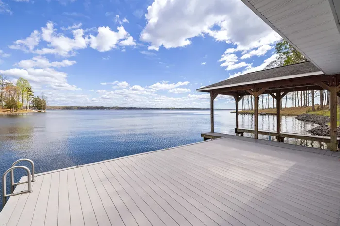 A spacious wooden dock extends over calm lake waters under a vast sky with fluffy clouds, offering a peaceful setting