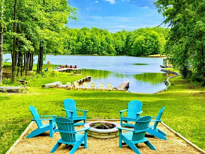 Lakeside fire pit area with colorful Adirondack chairs, offering serene water views and easy access to the private dock and beach
