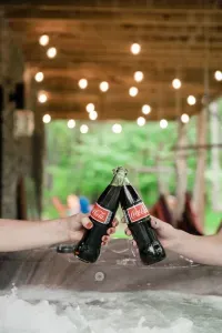 Cheers to camp memories! Raise an ice-cold Coke from the hot tub while hammocks sway and the firepit glows nearby — the perfect mix of playful nostalgia and mountain relaxation