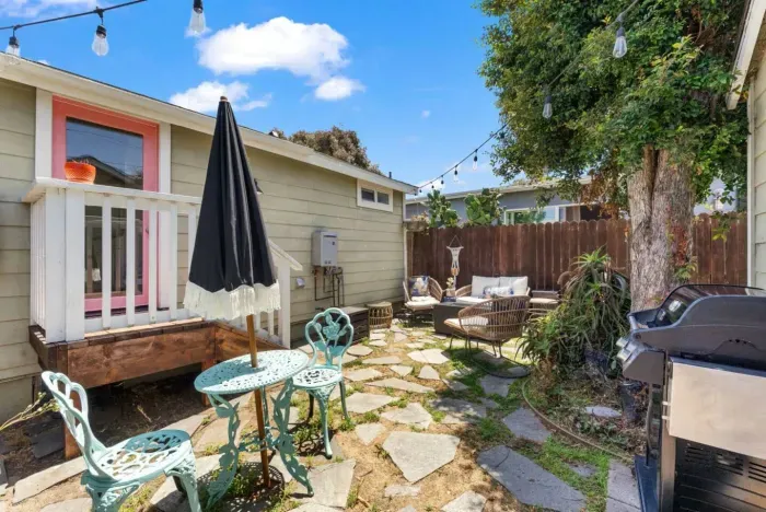 Colorful backyard retreat with BBQ grill, dining space, and cozy lounge area under string lights.