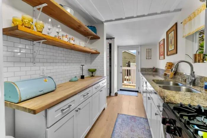 Charming galley kitchen with farmhouse vibes, featuring open shelving, butcher block counters, and a door to the sunny backyard deck.