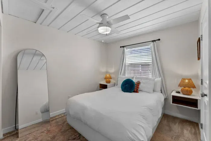 Serene bedroom with a full bed, warm rattan lamps, and a minimalist boho vibe accented by colorful throw pillows.