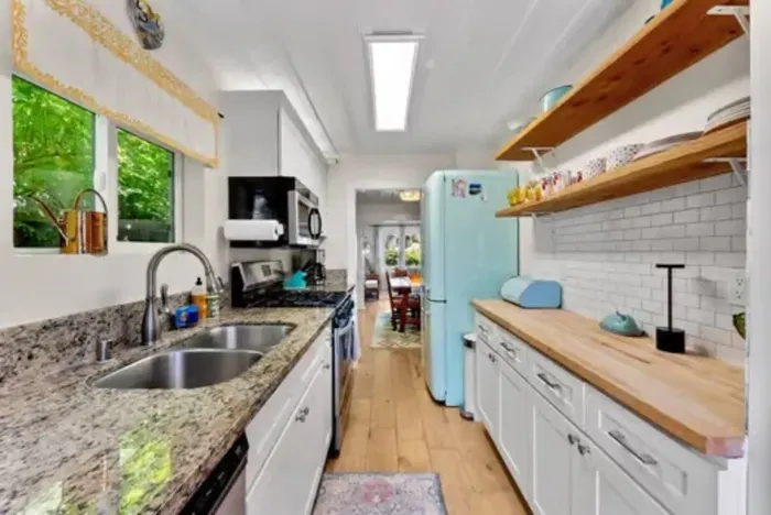 Bright galley kitchen with granite counters, open shelving, and a retro aqua fridge adding a fun pop of color.