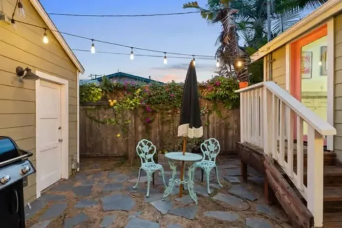 Charming patio with string lights, BBQ grill, and a bistro set—perfect for al fresco dining in a cozy garden setting.