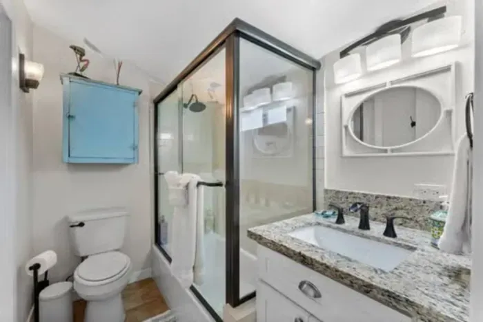 Stylish bathroom with granite vanity, glass-enclosed shower, and a pop of color from a vintage blue cabinet.