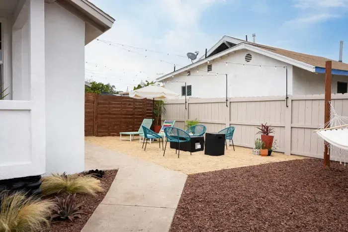 Private fenced yard with lounge chairs, fire pit seating, hammock, and string lights—perfect for relaxing day or night.