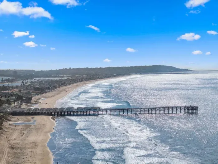 Waves curl beneath the pier under a bright coastal sky