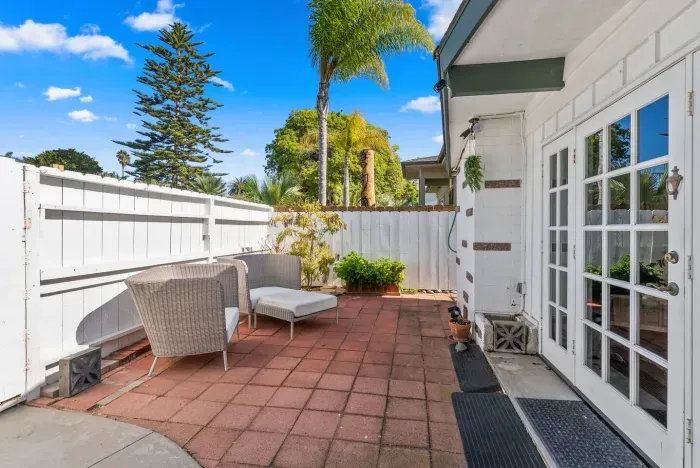 Red-tiled patio framed by palms and white fencing