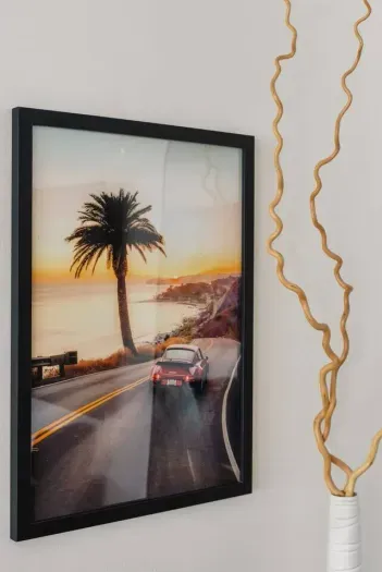 Framed artwork of a classic car on a coastal highway at sunset, adding nostalgia and adventure.