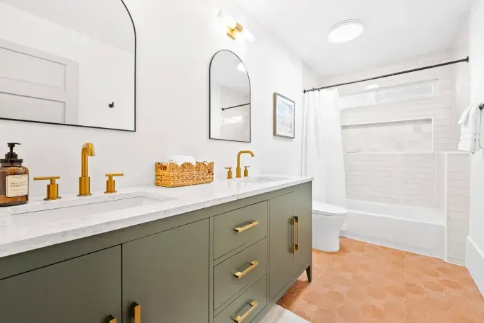 Modern bathroom with gold fixtures and dual mirrors.