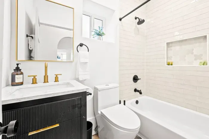 Clean modern bathroom with tub, gold accents, and bright tile.