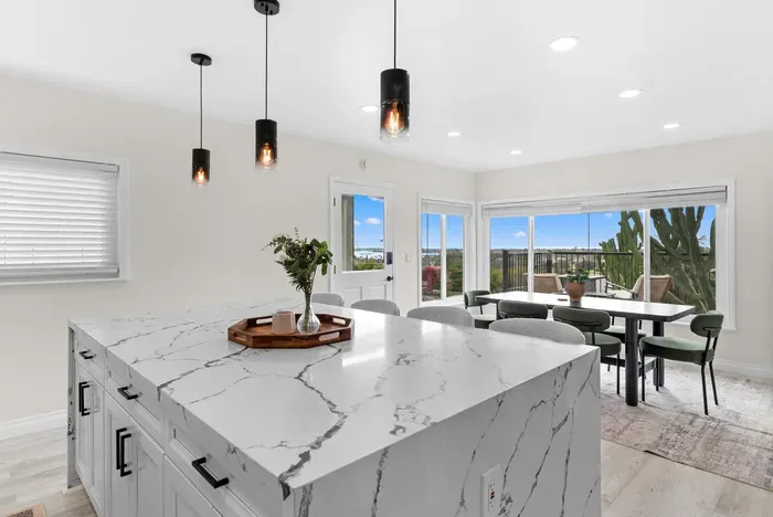Sunlit kitchen & dining with waterfall island, balcony and water views