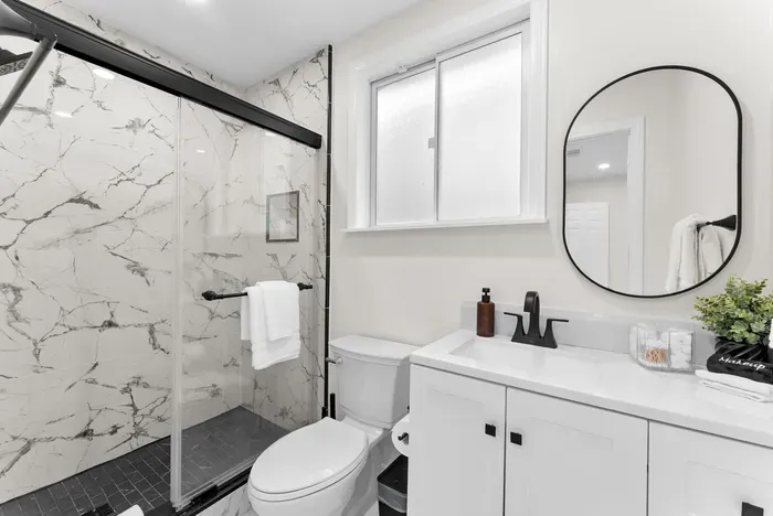 Sleek bath with marble shower, black fixtures & bright vanity