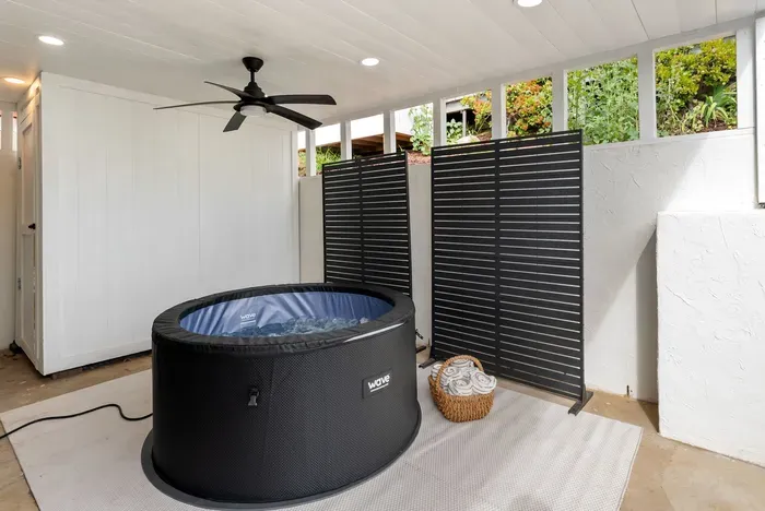 Covered spa nook with hot tub, privacy screens, towels, and fan