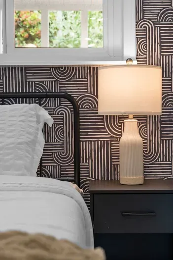Cozy bedside nook with modern wallpaper, soft lamp glow, and crisp linens