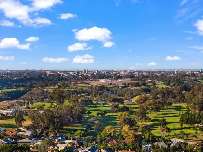wide scenic shot featuring nearby parkland and golf course greenery under a crisp blue sky.